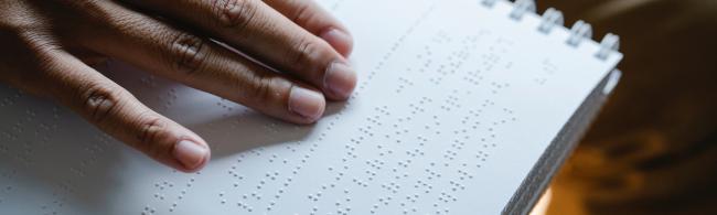 Eine blinde Person liest einen Text in Brailleschrift