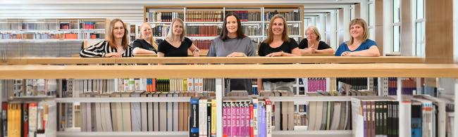 Sieben Personen stehen vor einem Bücherregal